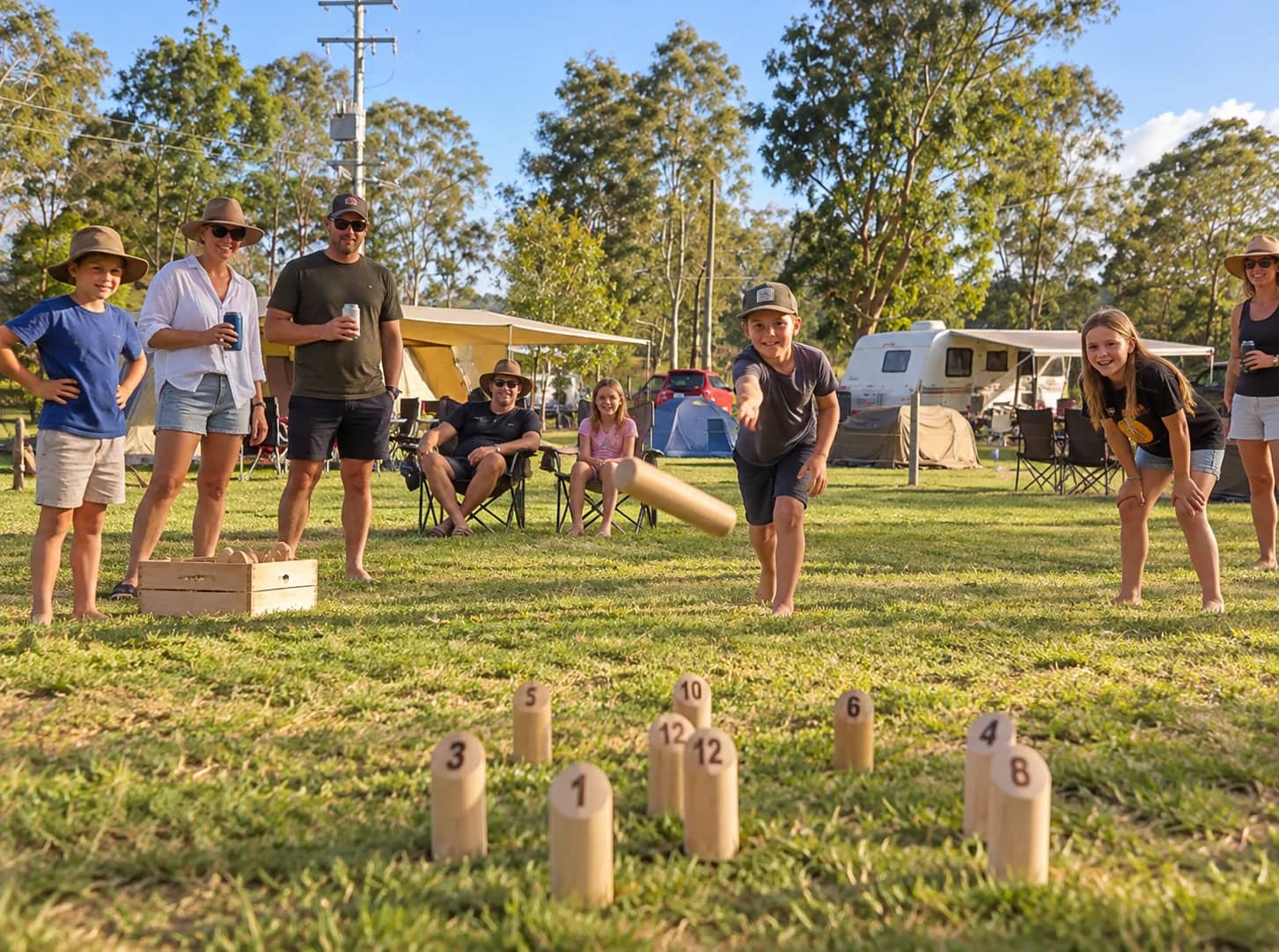 Families playing Mölkky on the grass, with tents and caravans set up behind them