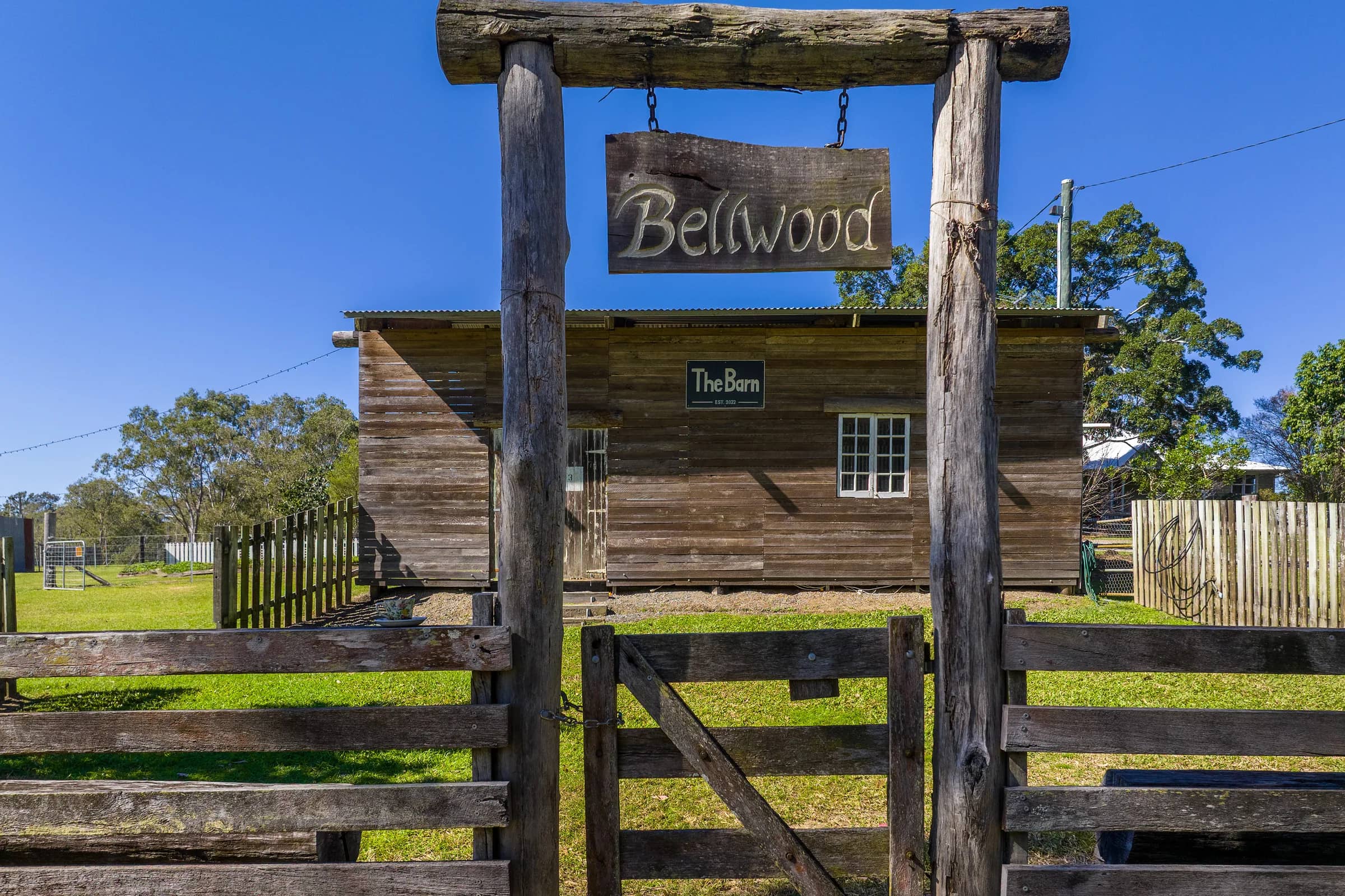 A carved Bellwood sign hanging over a timber gate, with The Barn behind it